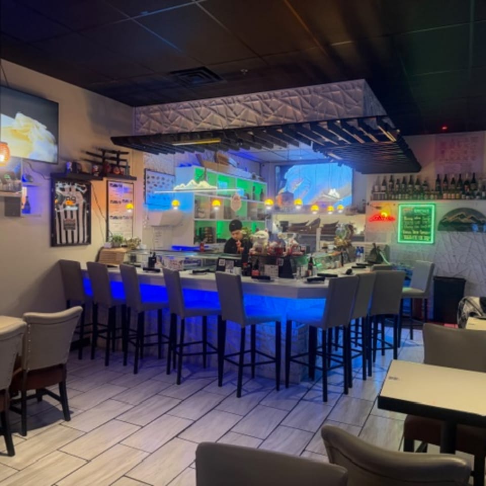 Interior of Sushi Yama with a sushi bar featuring blue underlighting and a chef preparing food.
