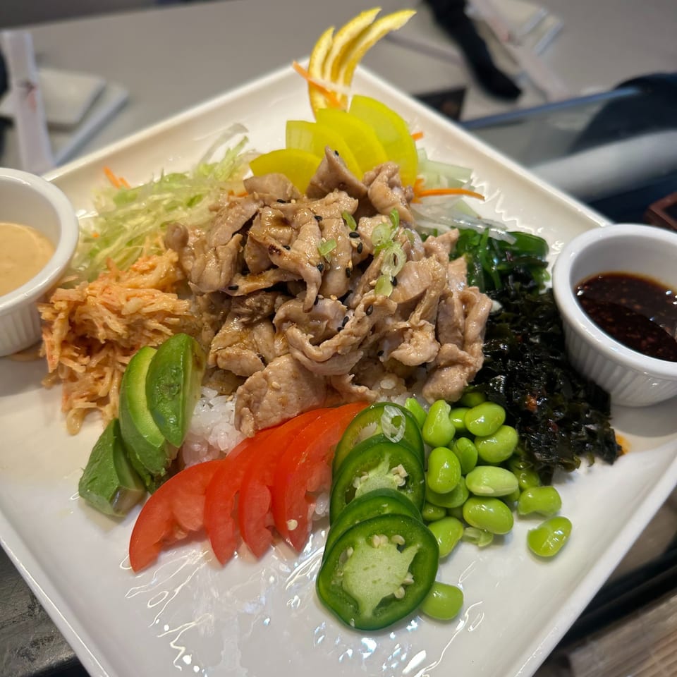 Japanese pork bowl with rice, avocado, tomatoes, edamame, seaweed, and pickled vegetables.