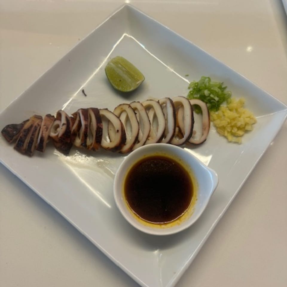 Grilled squid rings with a lime wedge, chopped scallions, ginger, and a dipping sauce.