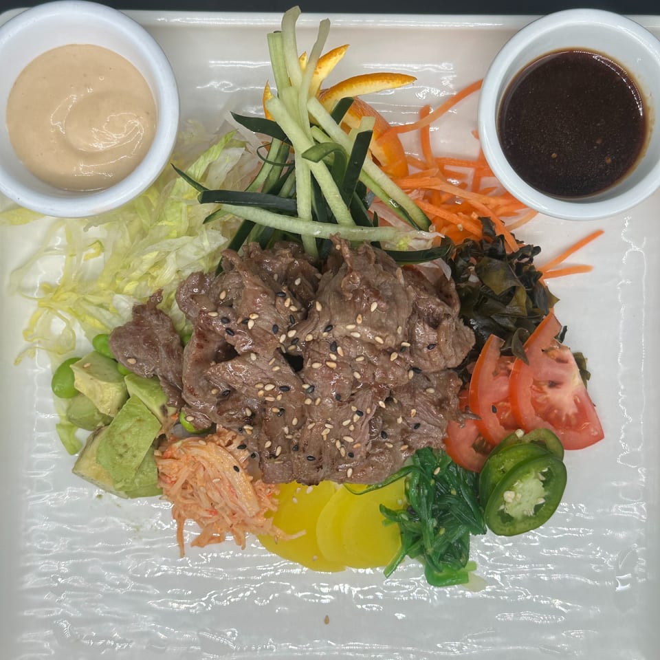 Japanese beef salad with avocado, seaweed, tomatoes, and sauces on a white rectangular plate.