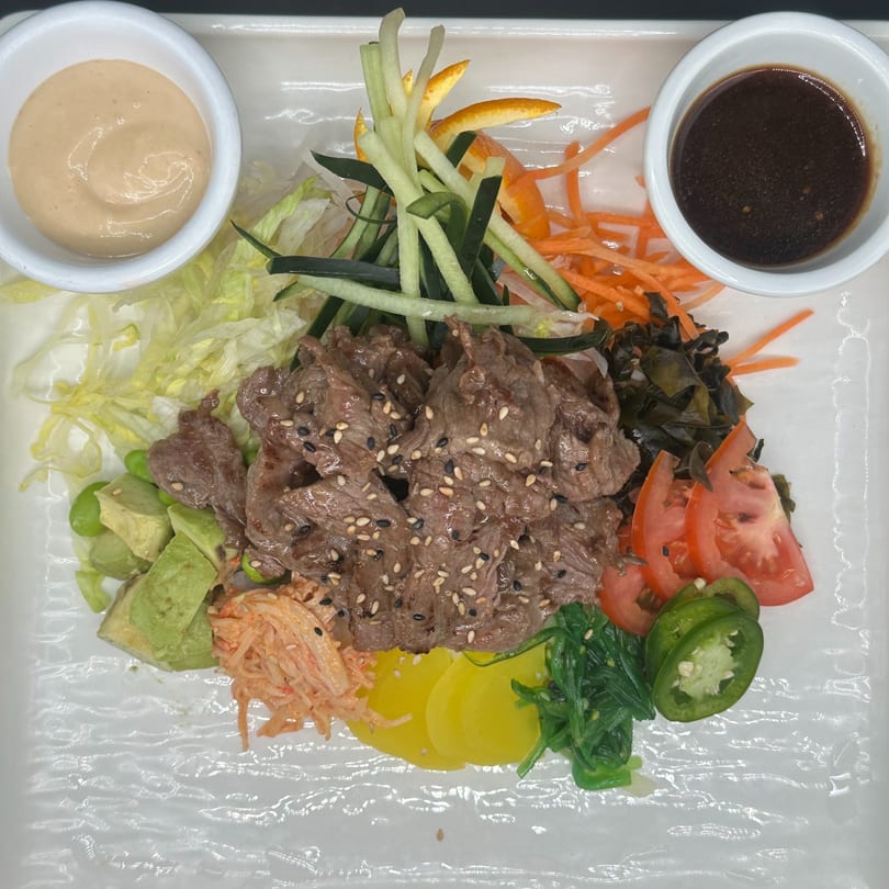 Japanese beef salad with avocado, seaweed, tomatoes, and sauces on a white rectangular plate.