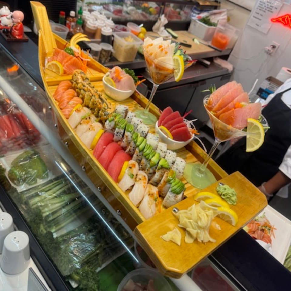 A large wooden boat filled with various sushi rolls, sashimi, and garnishes at Sushi Yama.