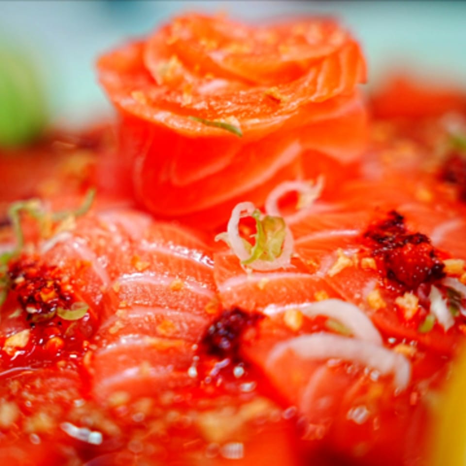 Close-up of vibrant red salmon sashimi slices, garnished with chili flakes and green onions.