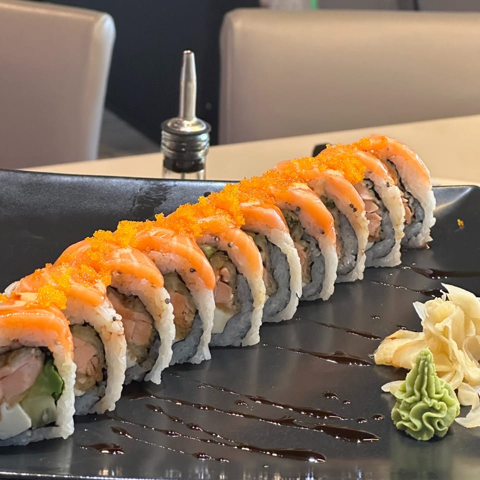 A long row of salmon sushi rolls topped with orange roe, served with ginger and wasabi.