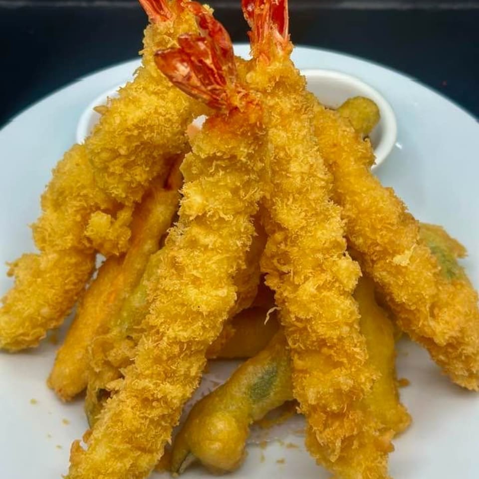 Golden-brown shrimp tempura with red tails and a side of dipping sauce on a white plate.