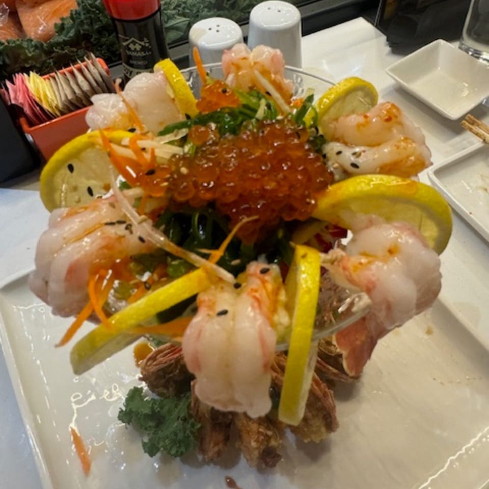 A Japanese seafood salad with shrimp, salmon roe, seaweed, and lemon slices on a white plate.