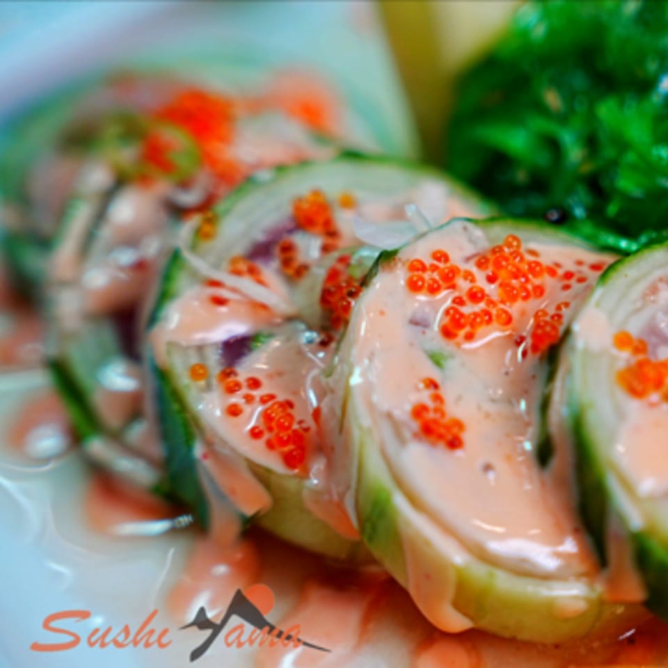 Close-up of Sushi Yama's sushi rolls, topped with creamy sauce and bright orange roe.