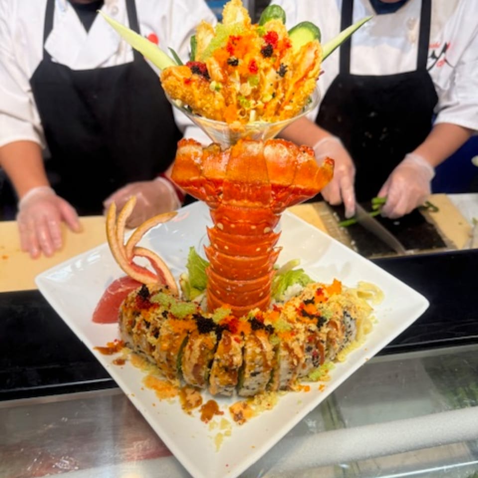A large sushi roll with a lobster tail and a martini glass of tempura shrimp, prepared by chefs.