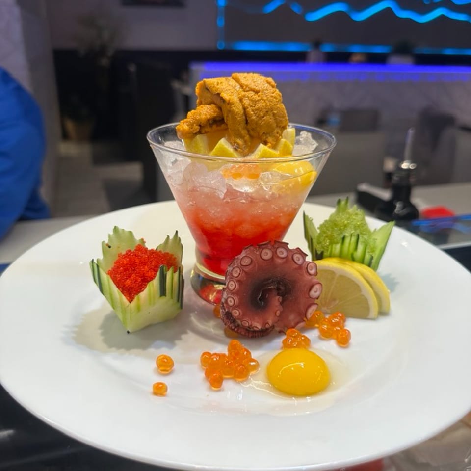 A Japanese seafood dish with uni, octopus, roe, and a red cocktail in a martini glass.