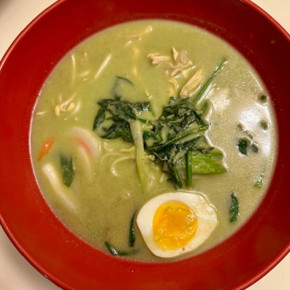 A red bowl of green ramen with chicken, spinach, noodles, and a hard-boiled egg.