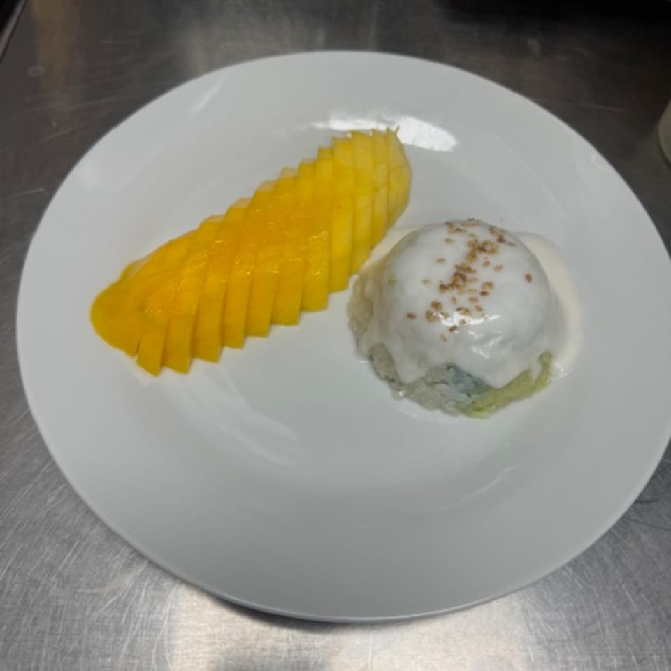 Sliced mango and sticky rice with coconut milk and sesame seeds on a white plate.