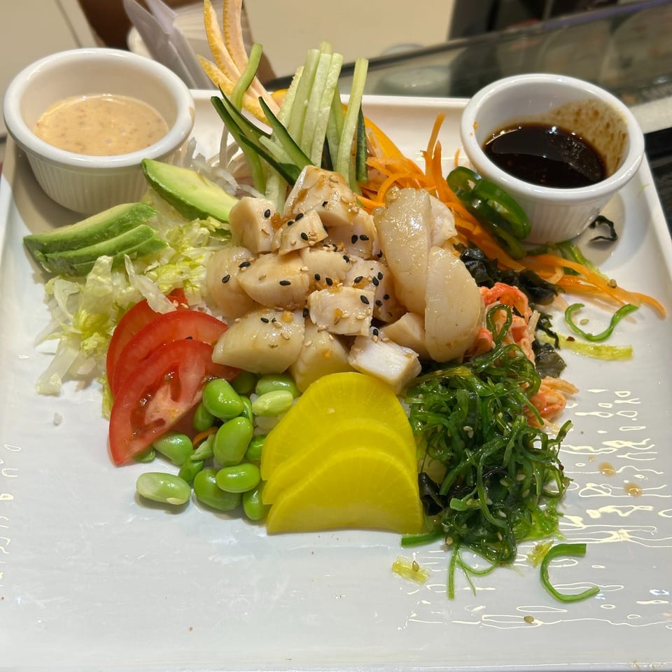 Japanese scallop salad with avocado, edamame, seaweed, and two dipping sauces on a white plate.