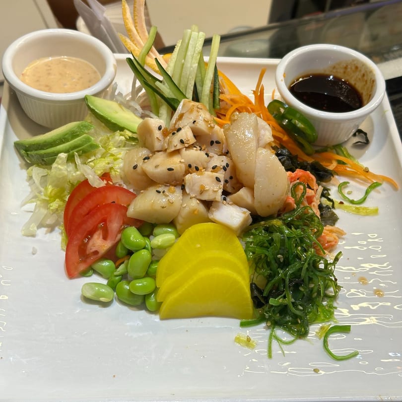 Japanese scallop salad with avocado, edamame, seaweed, and two dipping sauces on a white plate.