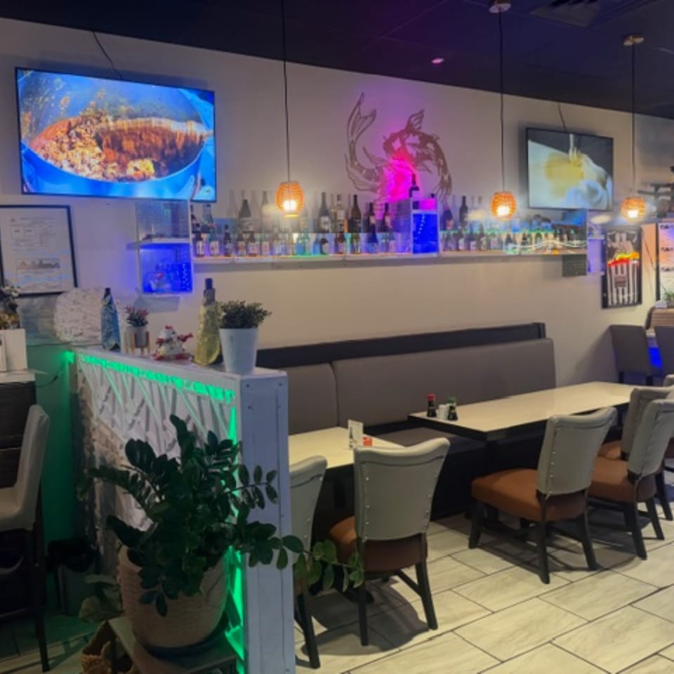 Interior of Sushi Yama restaurant with tables, chairs, a bar, and TVs displaying food.