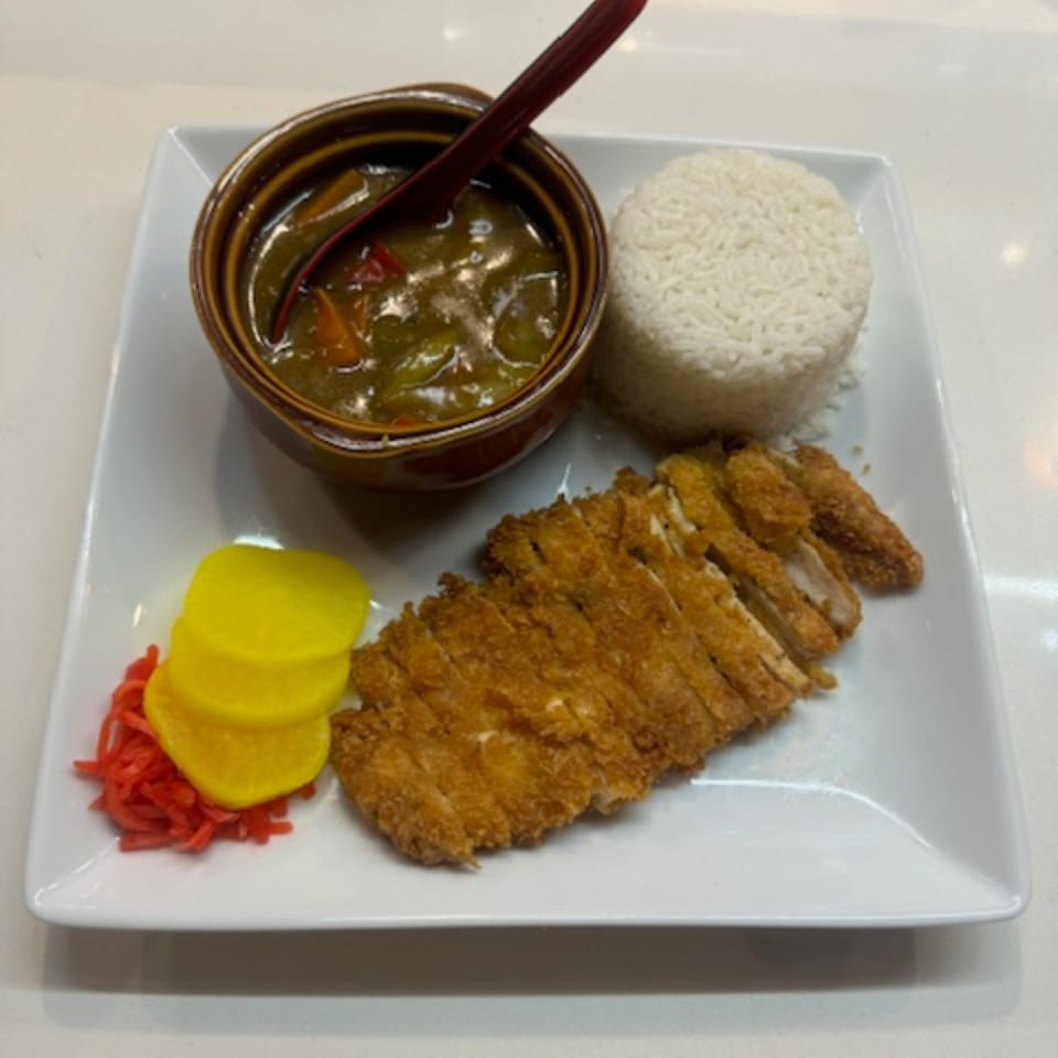 Japanese chicken katsu curry with rice, yellow pickled daikon, and red ginger on a white plate.