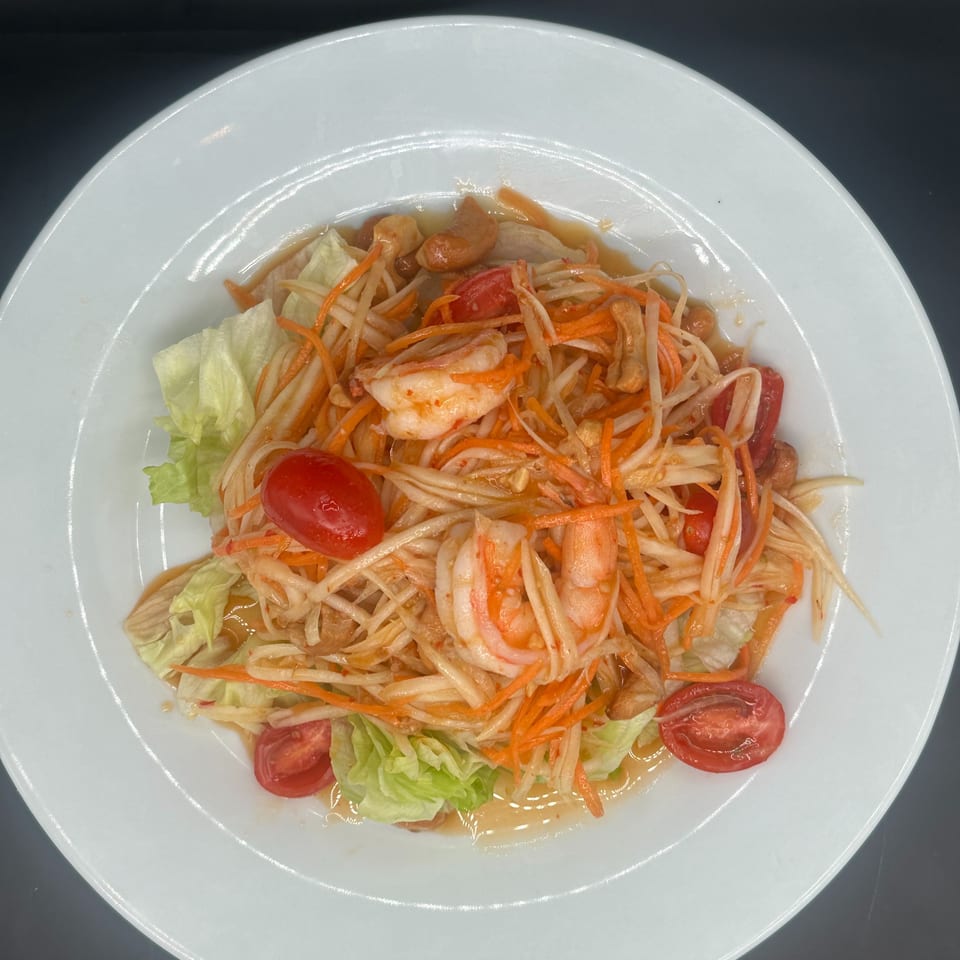 A vibrant papaya salad with shrimp, cherry tomatoes, cashews, and shredded carrots on a white plate.