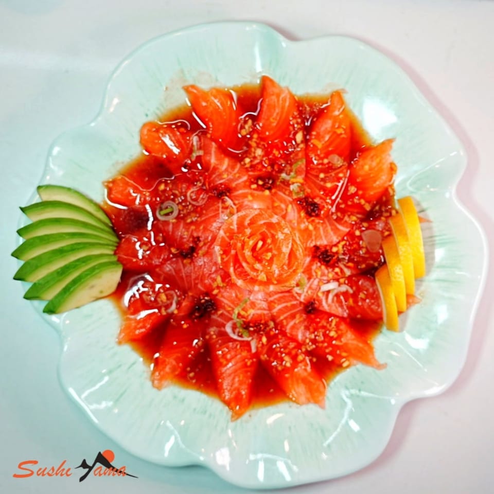 Sushi Yama's salmon sashimi, artfully arranged with avocado and lemon slices on a light blue plate.