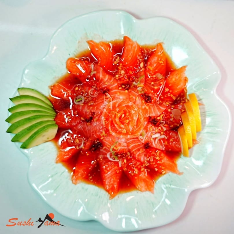 Sushi Yama's salmon sashimi, artfully arranged with avocado and lemon slices on a light blue plate.