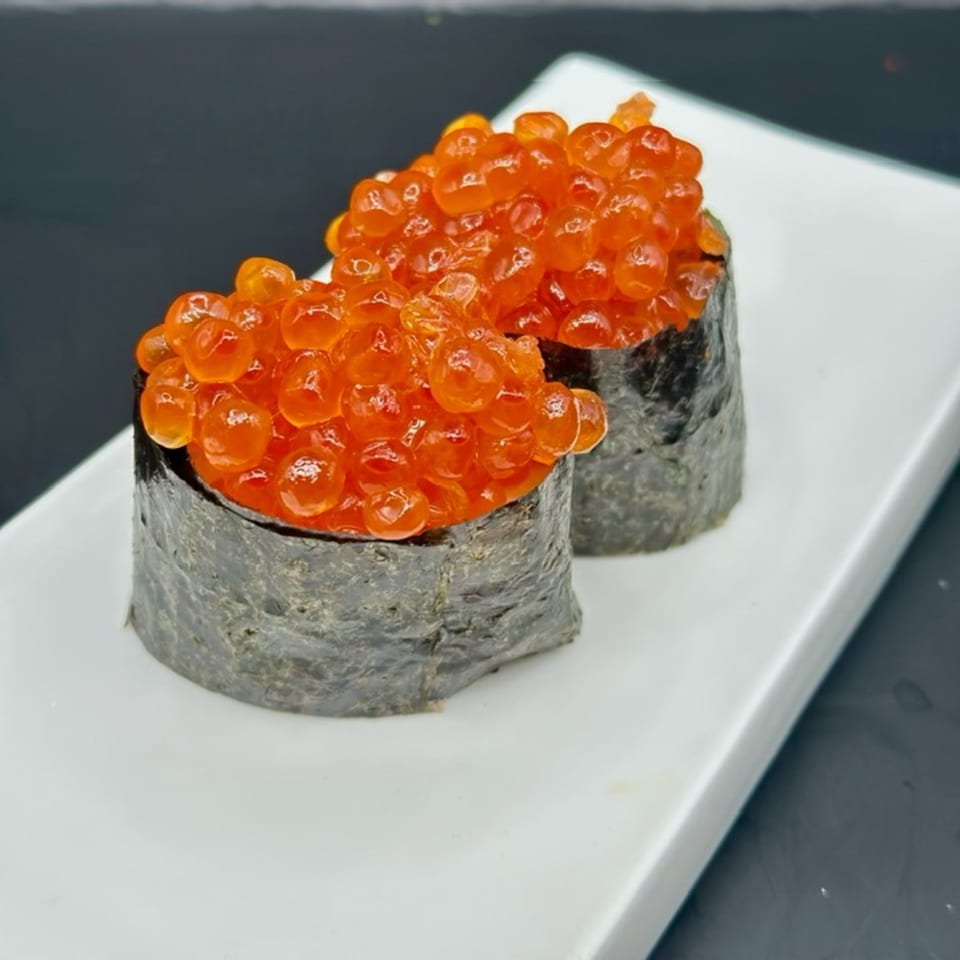 Two vibrant orange salmon roe (ikura) gunkan maki sushi pieces on a white rectangular plate.