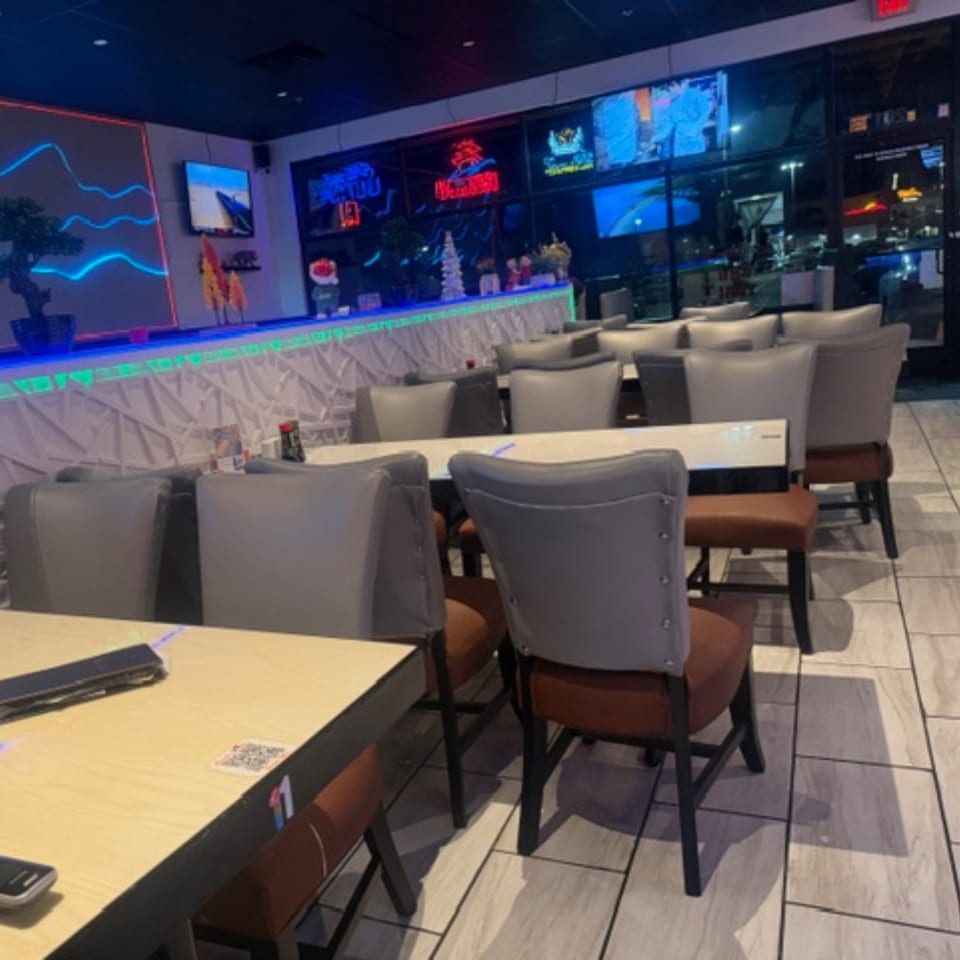 Interior of Sushi Yama restaurant with empty tables and chairs, neon lights, and TVs on the wall.