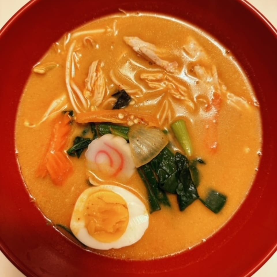 A vibrant red bowl of Japanese ramen with chicken, vegetables, fish cake, and a hard-boiled egg.