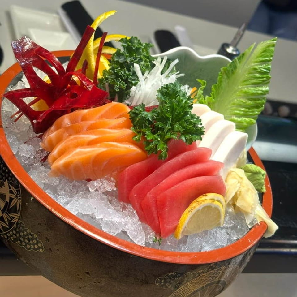 A colorful sashimi platter with salmon, tuna, and white fish, garnished with lemon and greens on ice.