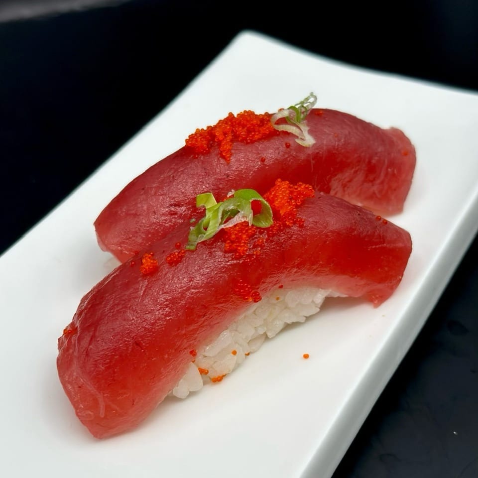 Two pieces of tuna nigiri sushi, topped with red tobiko and green onions, on a white plate.