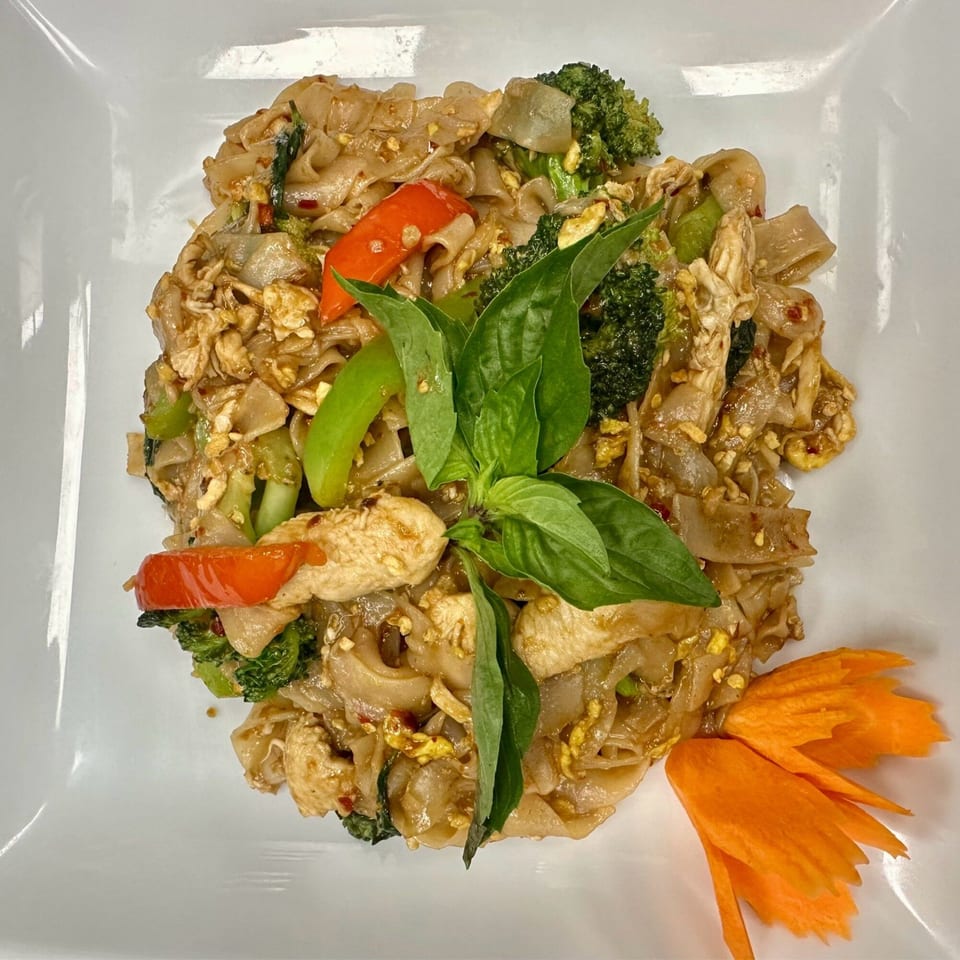 Pad See Ew with chicken, broccoli, red peppers, and basil, garnished with a carrot flower.