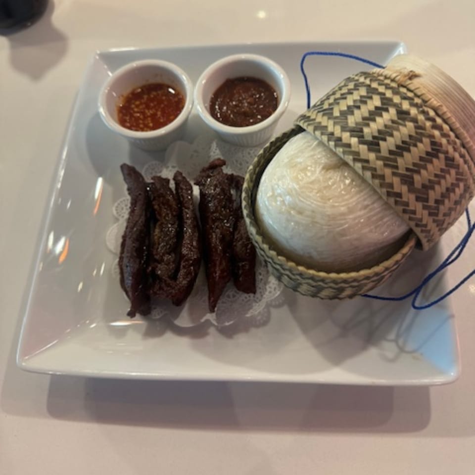 A plate with dark meat strips, two dipping sauces, and sticky rice in a woven basket.