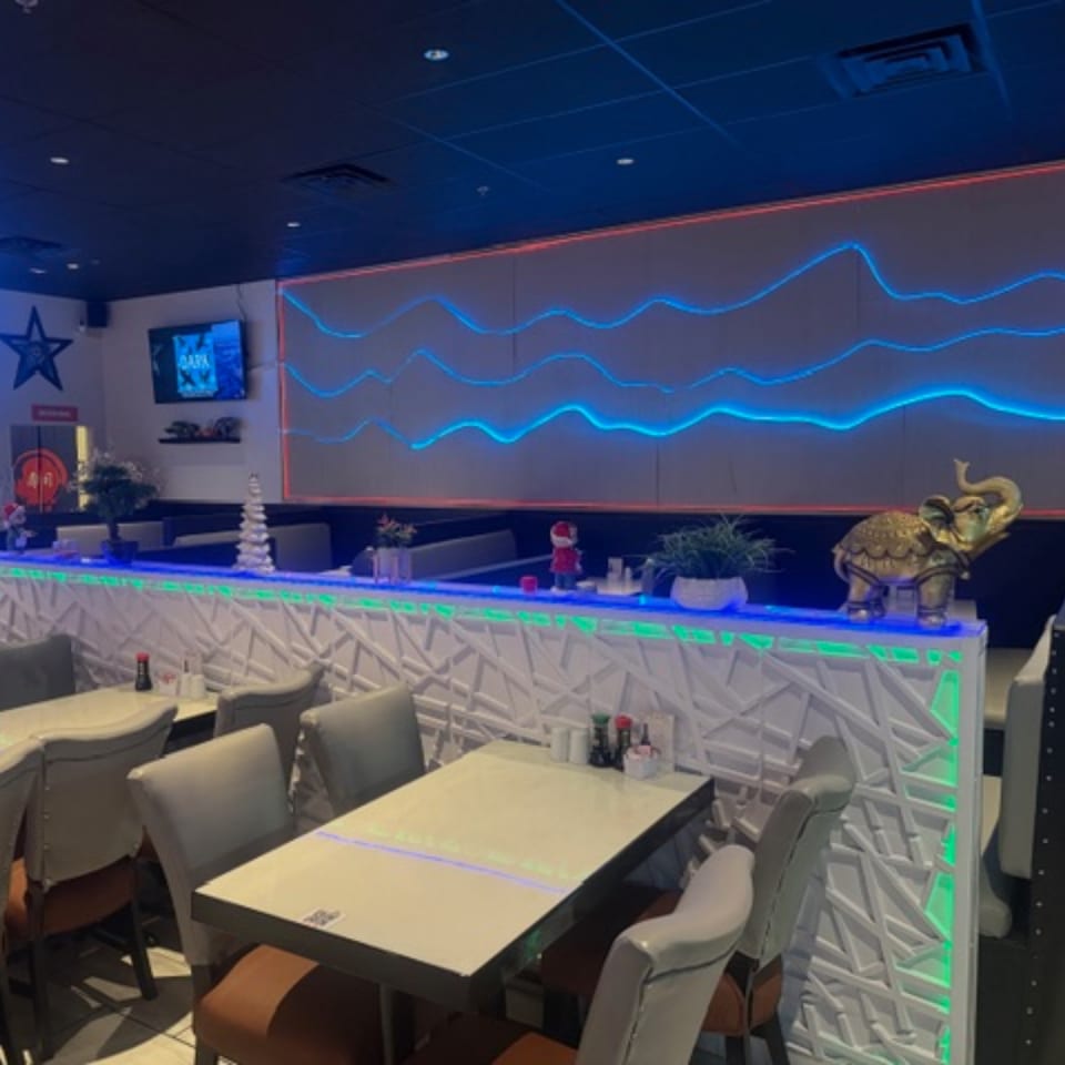 Sushi Yama's dining room features modern decor with blue and green neon lighting and white tables.